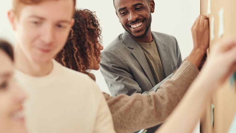 A diverse group of professionals collaborating on a project by using sticky notes on a board indoors.